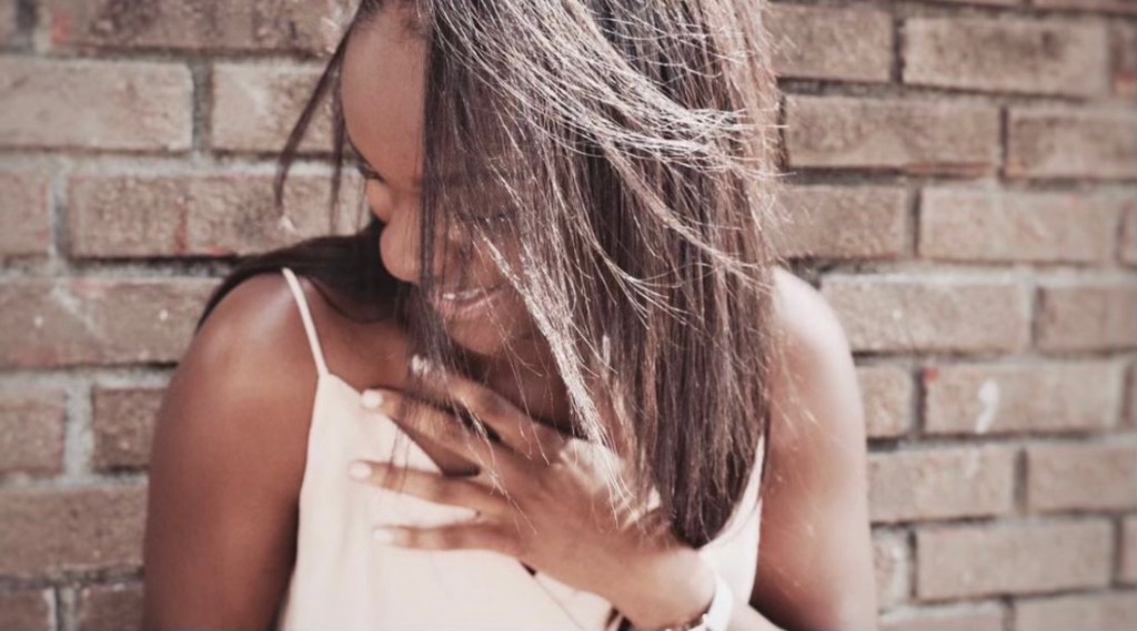Christian "CJ" Jordan clutching her chest in laughter in front of brick wall in Birmingham, AL